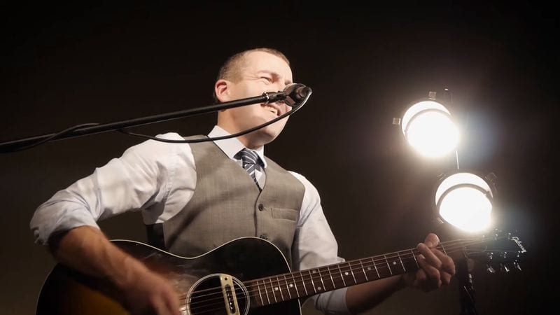 Darren Scott performing live with guitar under stage lighting